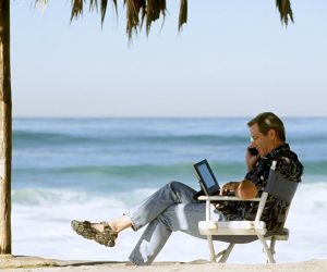 man using laptop and phone on beach